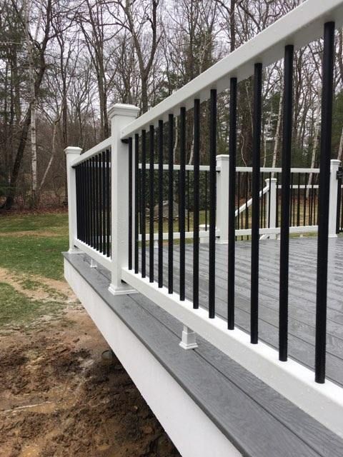 White deck railing with black vertical spindles, overlooking a yard and trees.