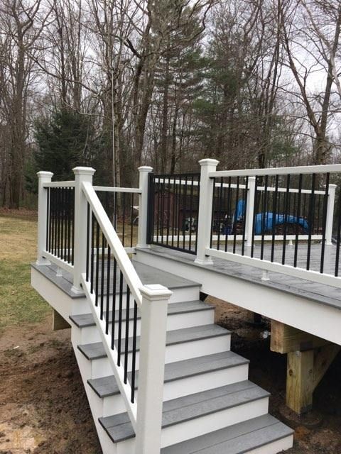 White and gray deck with black railings and steps leading to a yard with trees.