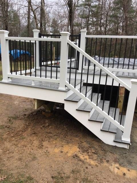 White deck with gray steps and black railings, in a muddy yard.
