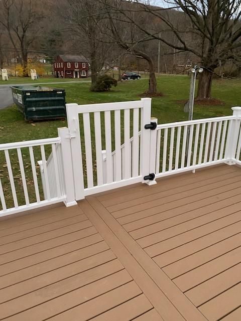 White deck with a gate and railing, brown composite decking. Green trash bin and red building in the background.