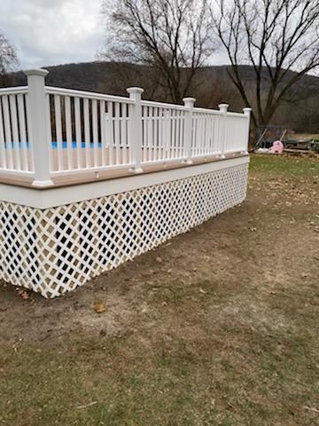White deck with lattice skirting, overlooking a yard with a pool.