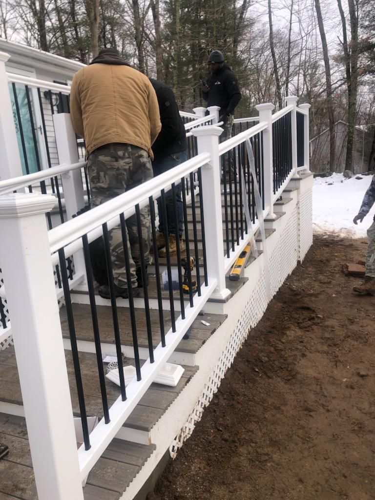 Workers installing railing on outdoor steps; white posts, black spindles, tan jackets.
