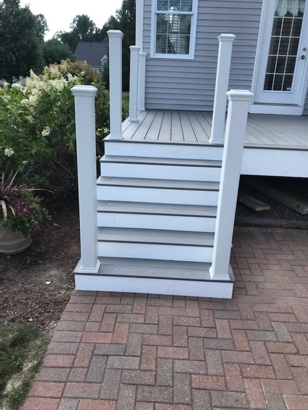 Gray composite steps leading up to a deck with white posts. Brick patio in front.