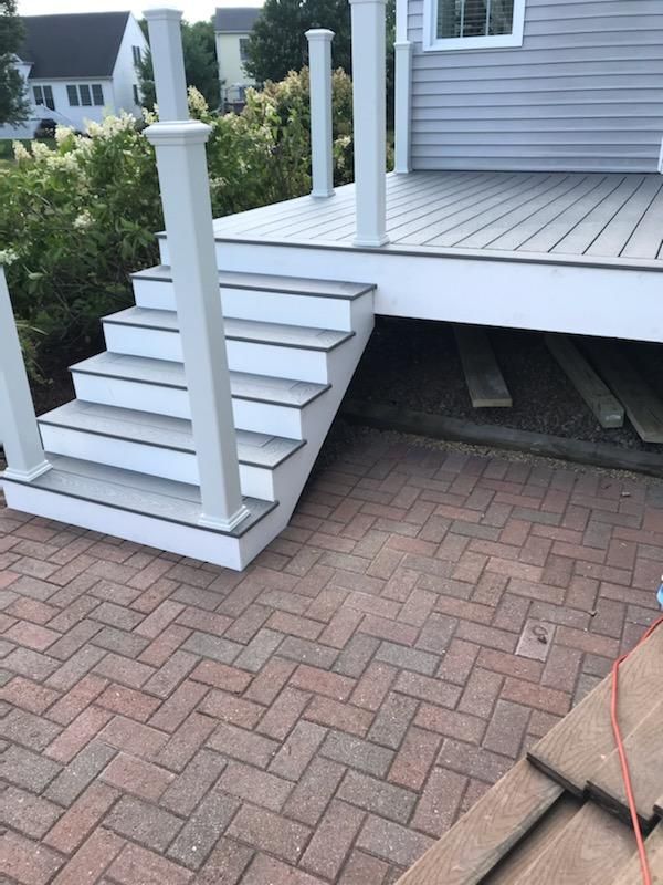 A deck with white stairs and railings leads down to a brick patio.