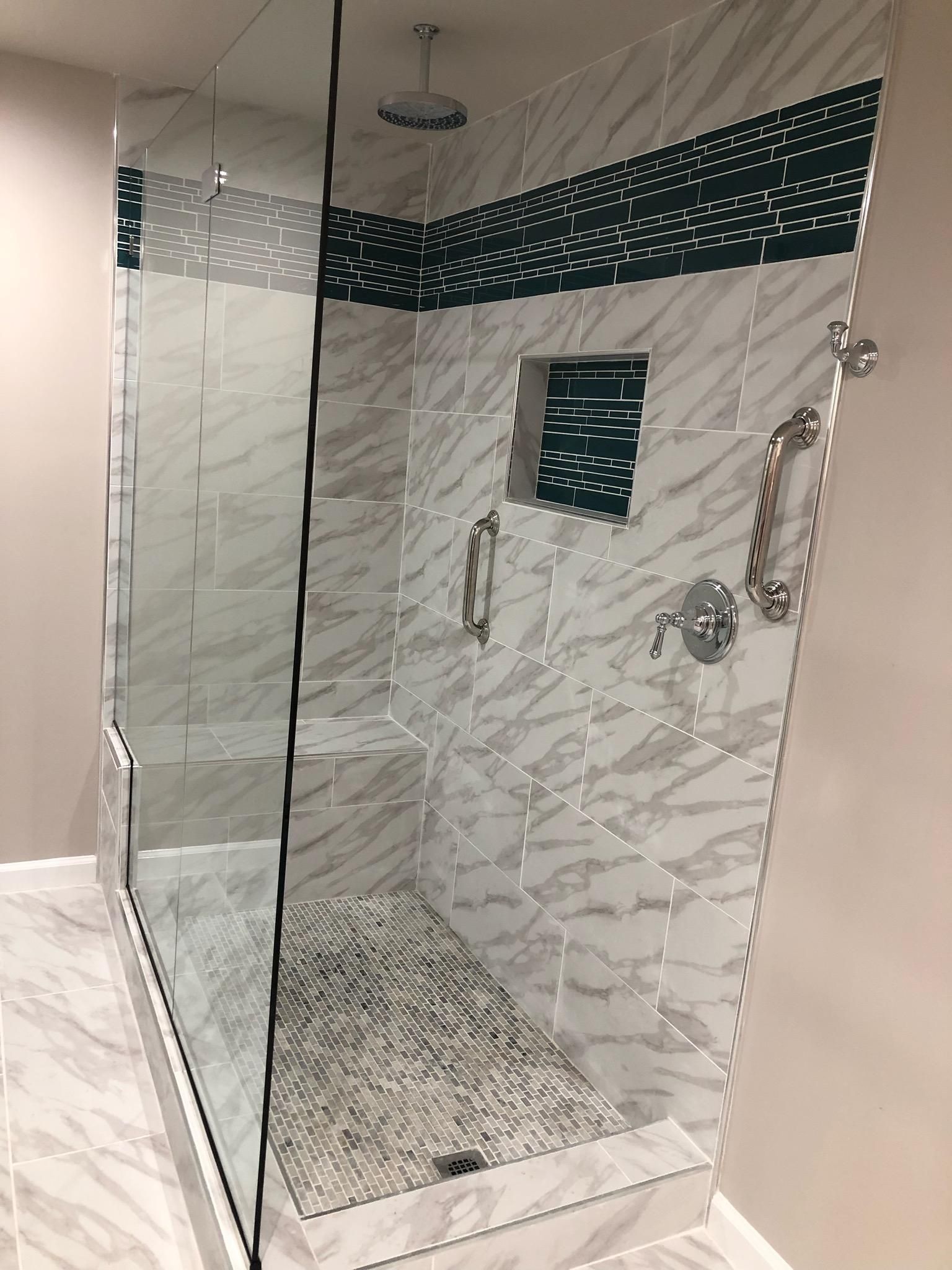 Shower stall with glass door, marble tiles, dark green accent, chrome fixtures.