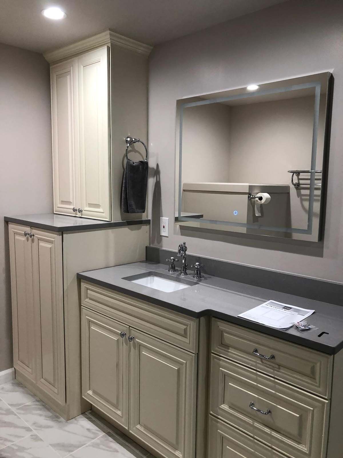 Bathroom with cream cabinets, gray countertop, mirror, and toilet paper holder.