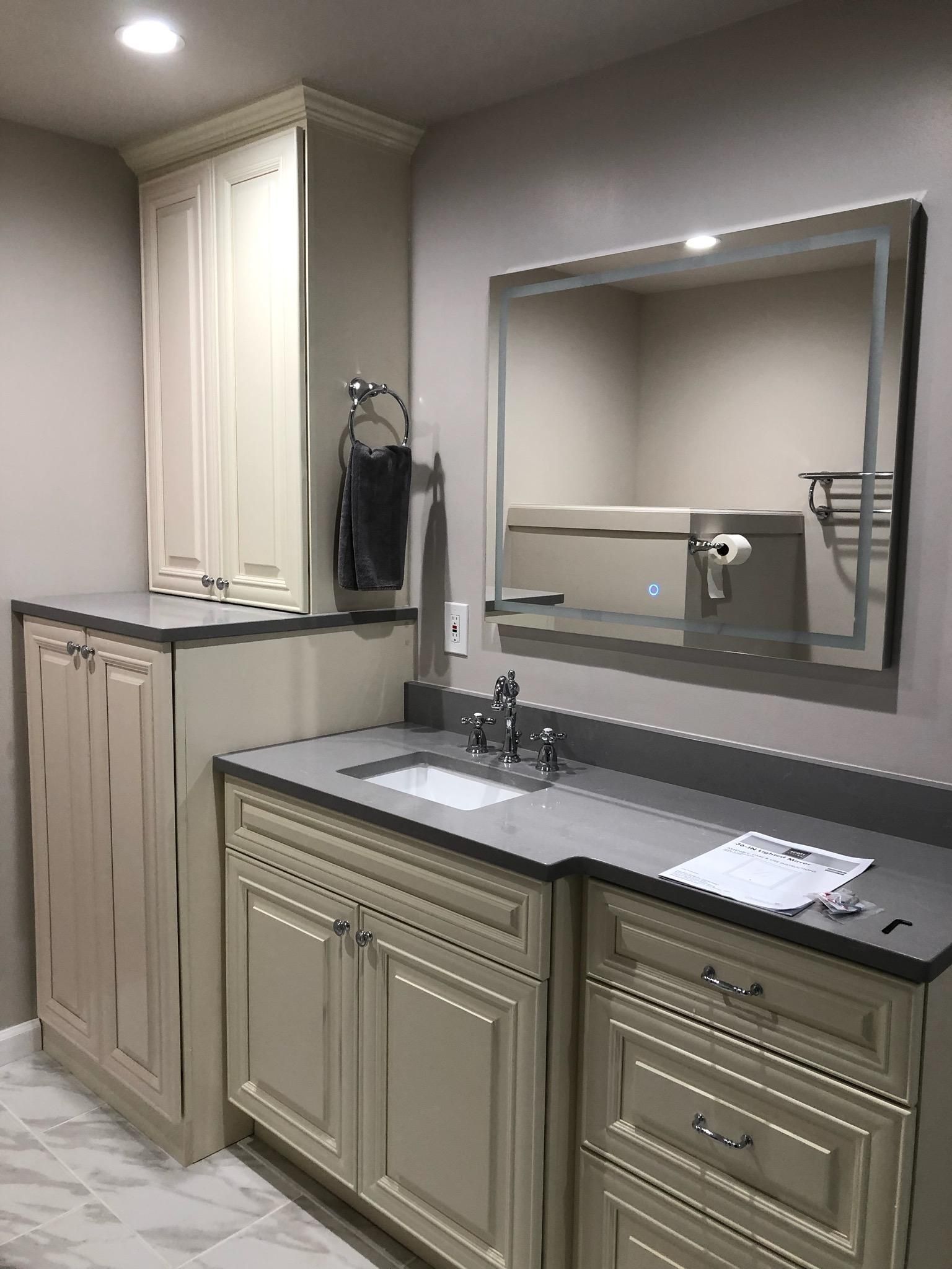 Bathroom with off-white cabinets, gray countertop, square mirror, and towel rack.