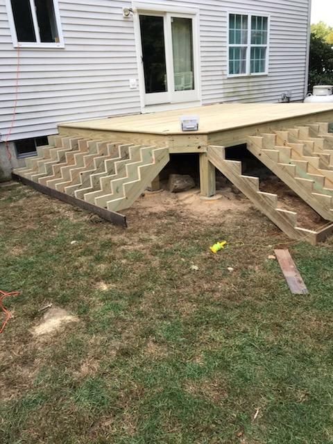 Newly constructed wooden deck with steps leading down to a grassy yard, attached to a light-colored house.