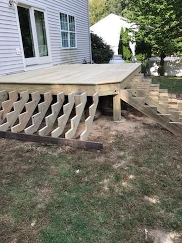 Wooden deck with stairs leading to a grassy yard. Gray house in background.