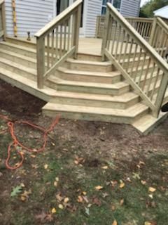 Wooden deck with steps and railings leading down to a grassy yard.