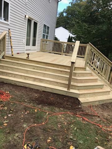 Wooden deck with stairs leading down to a yard, attached to a light-colored house.