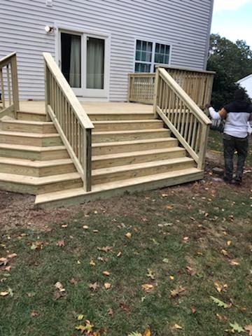 Wooden deck with stairs leading to a house with a sliding glass door; a person stands nearby.