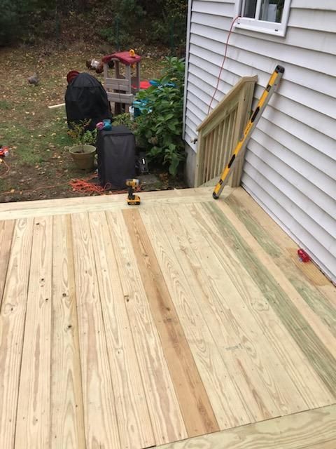 Newly built wooden deck next to a white house with stairs and a level leaning against the railing.