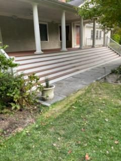 A porch with multiple steps leading to a house, with white columns, stone pathway, and greenery.