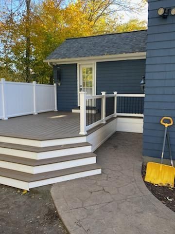 A blue-sided building with a deck and steps, and a concrete path. A yellow shovel leans against the side.