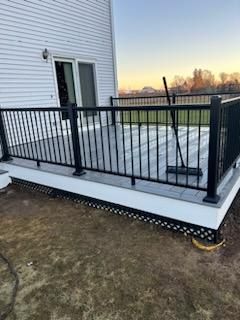 Newly built gray composite deck with black railing and white trim on a house with a door.