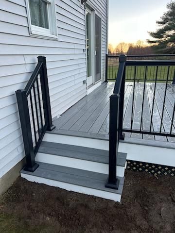 Gray deck with steps, black railing, and sliding glass door on a white house.