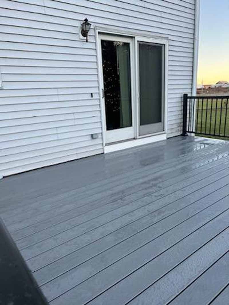 Gray painted deck with sliding glass door and black railing against a white siding house.