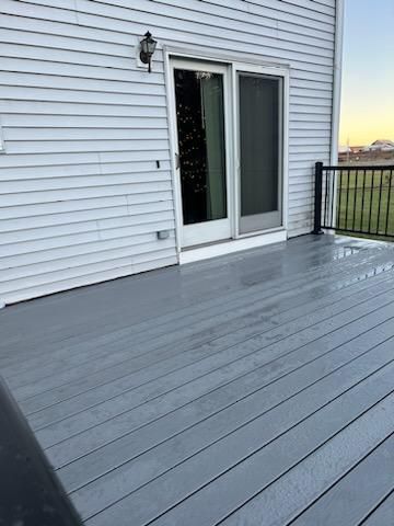 Gray painted deck with sliding glass door and black railing. House exterior with white siding.