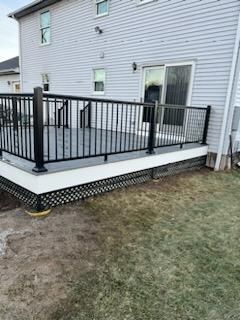 Black and white deck with railings attached to a light gray house, viewed from the yard.