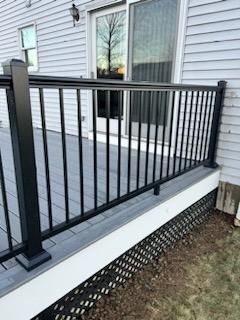 Black railing on a gray deck next to a house with a sliding glass door and lattice skirting.