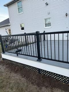 Gray composite deck with black railing and white trim. Lattice skirting. House in background.