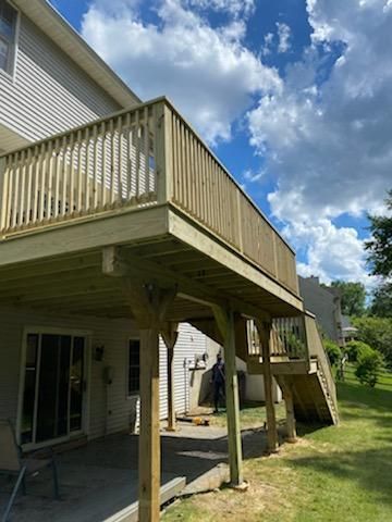 Wooden deck with railing, supported by posts. Stairs lead to the lower level. Cloudy blue sky.