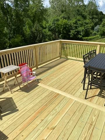 Wooden deck with railing, a small table, a child's chair, and a table with chairs in a wooded setting.