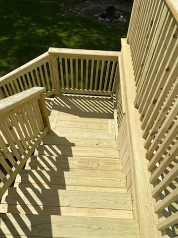Wooden deck stairs with railings, casting shadow on the steps. Bright, sunny outdoors.