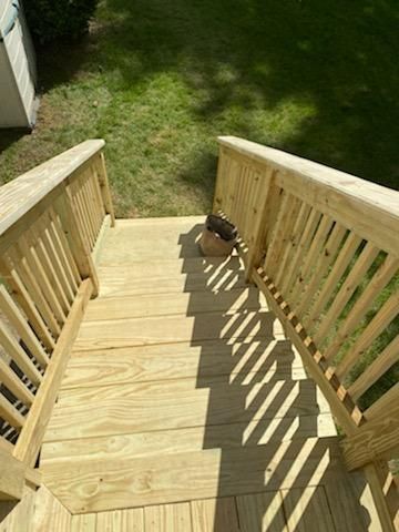 Wooden outdoor stairs with railings leading to a grassy yard.