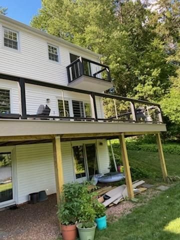 Two-story house with a large deck and small balcony. Black railings, white siding, and green yard.