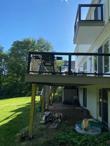 A two-story deck on a white house with black railings, overlooking a green lawn.