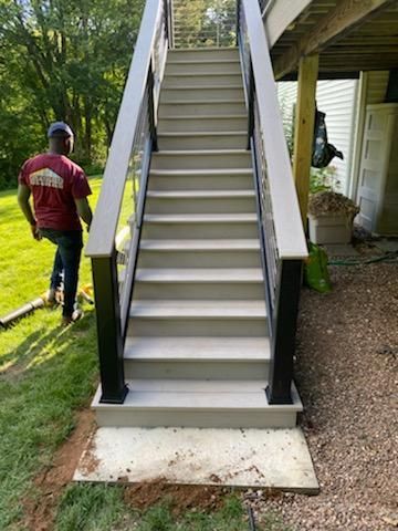 Outdoor staircase with gray steps and black railings, leading up to a deck. A person walks near the stairs.