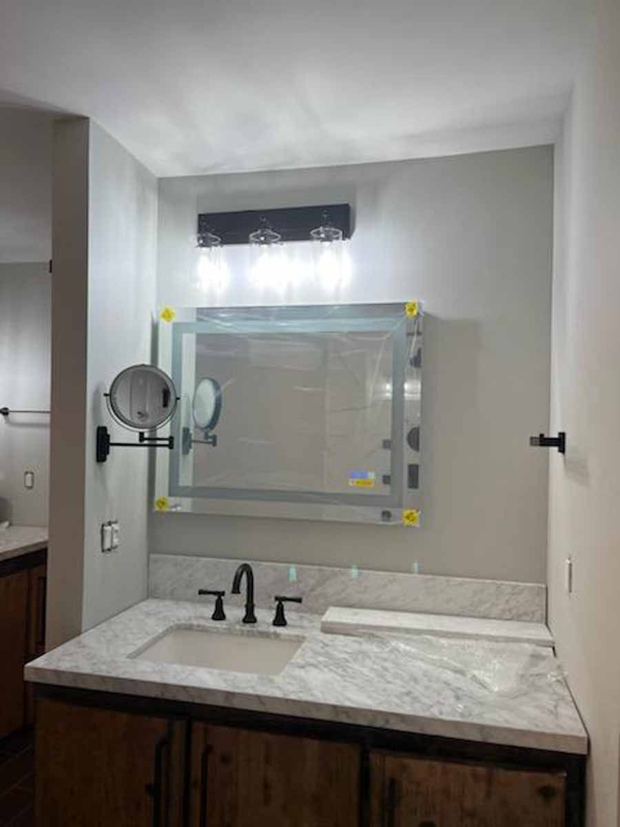 Bathroom vanity with a rectangular mirror, sconce lighting, and a marble countertop.