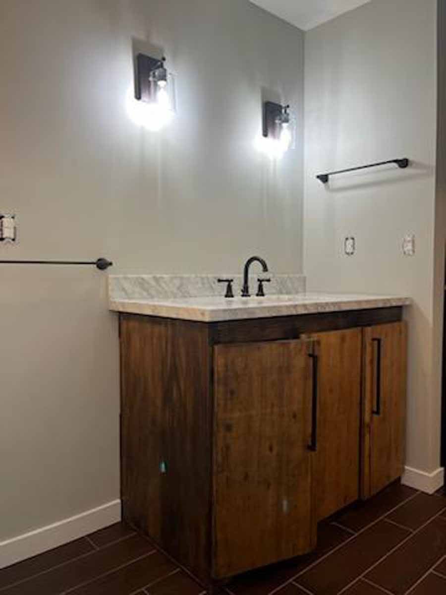 Bathroom with wood vanity, marble countertop, black fixtures, and two sconce lights.