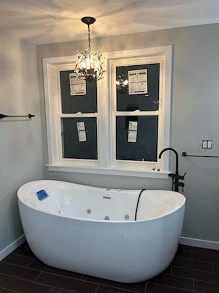 Bathroom with a white freestanding tub below a window. A chandelier hangs above the tub.