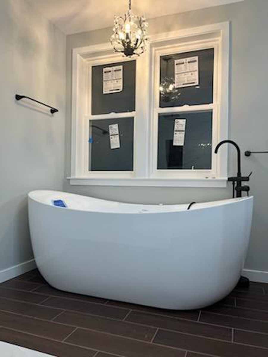 White bathtub in a modern bathroom with dark brown floor tiles and two windows.