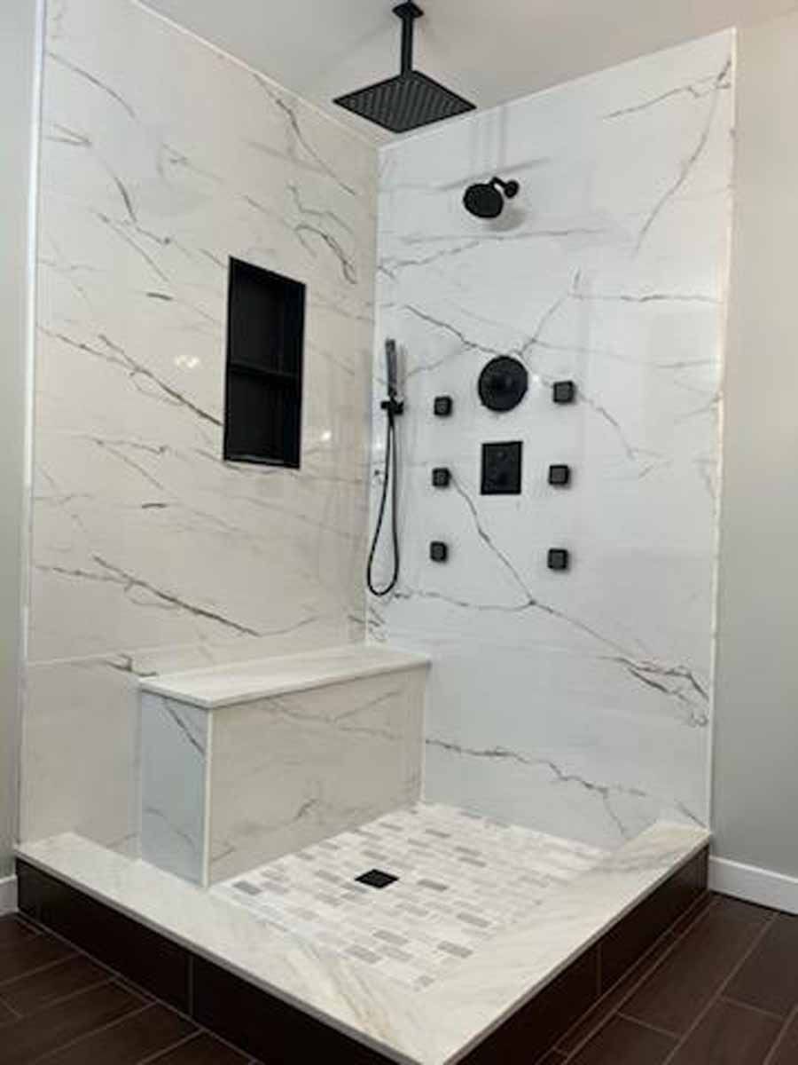 Modern white marble shower with black fixtures and built-in bench.