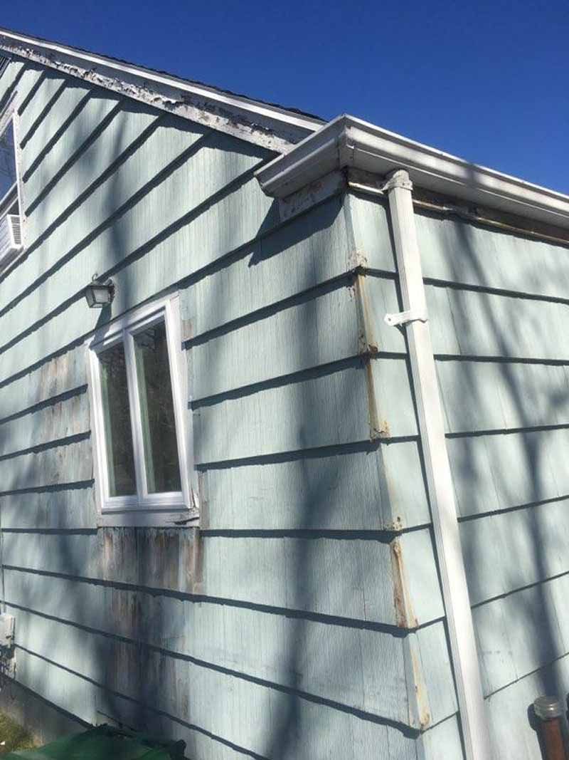 Side of a light blue house with a white window and gutter, showing dirt stains on the siding.