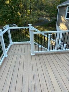 Wooden deck with white railing, black spindles, and view of trees.