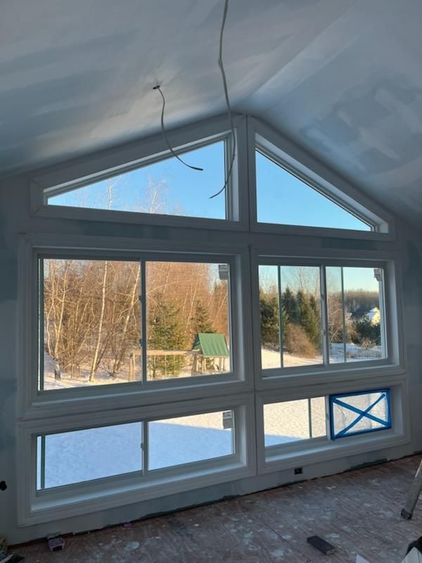 Large, white-framed windows on a snow-covered exterior with a triangle top. Inside a room with light walls and some wiring.