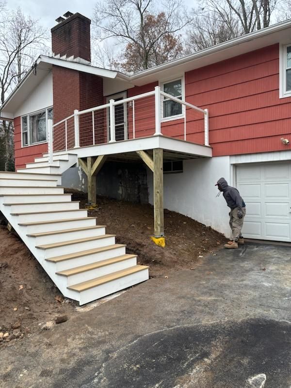 House with deck, stairs. Red siding, white railing, gray driveway, person inspecting.
