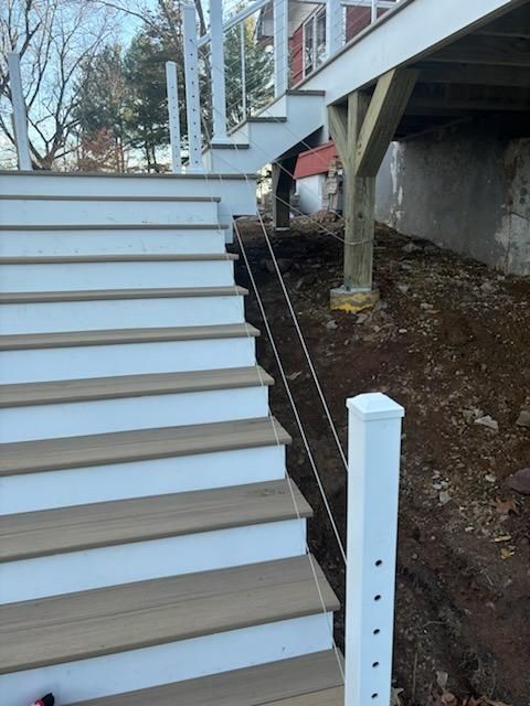 Outdoor staircase with white risers, composite treads, and cable railing; construction site.