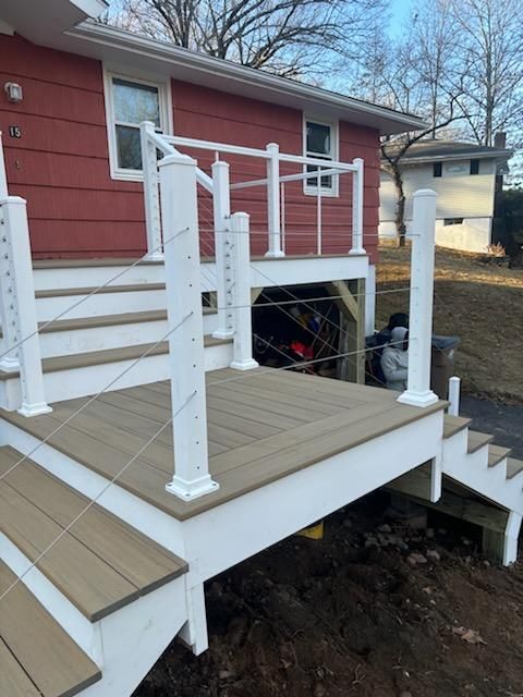 White-railed deck with cable infill and composite decking, attached to a red house. Staircase descends to the right.