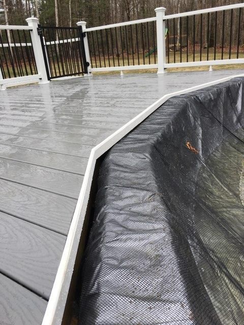 A black tarp liner outlines the edge of a pool, with gray decking and a white railing in the background.