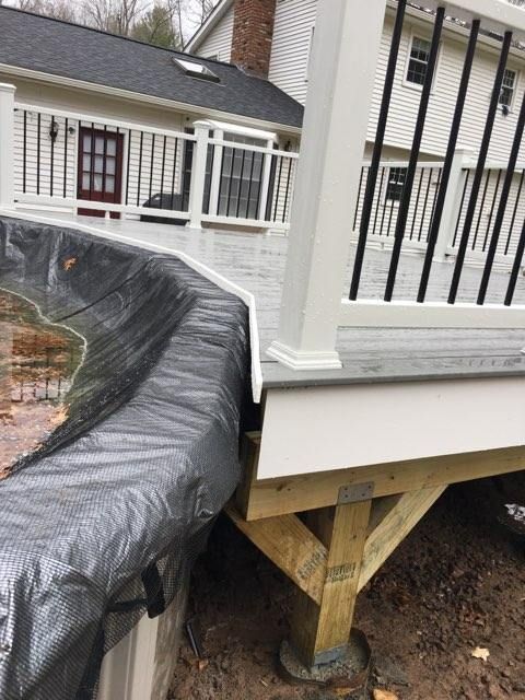 Partially constructed deck with black tarp draped over a curved retaining wall.