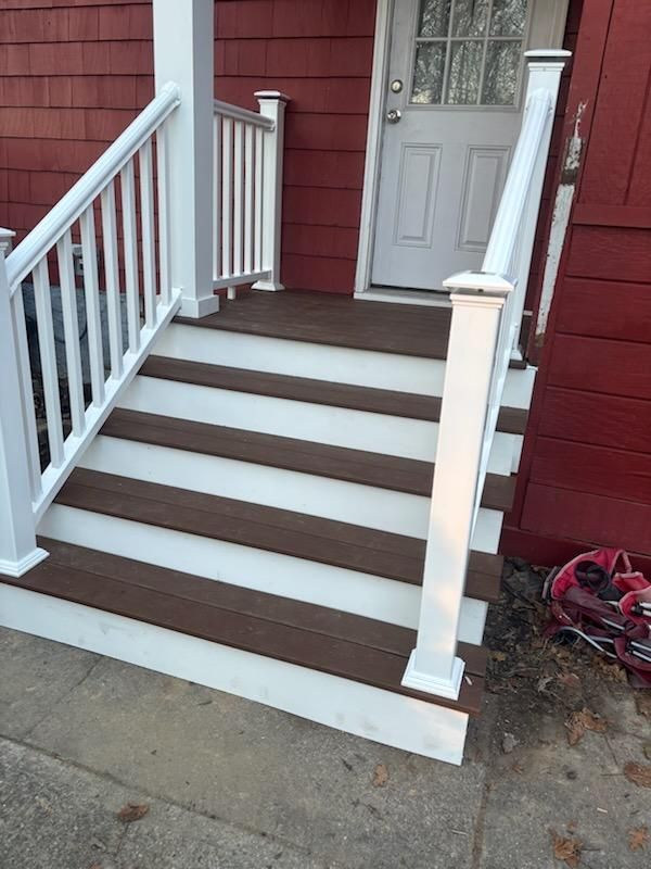 Brown and white deck stairs leading to a white door, set against a red building.