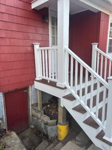Red house entrance with white railing and stairs. Steps lead up to a doorway and porch.