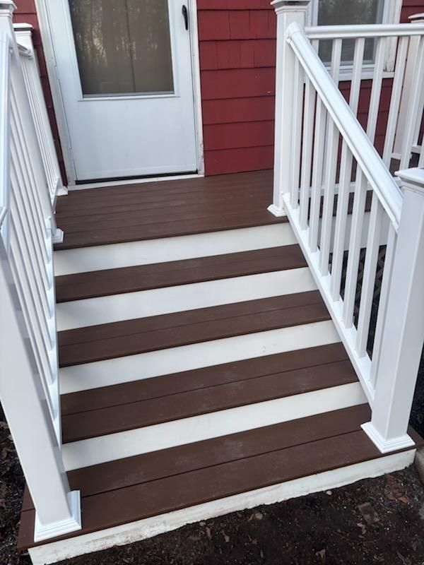 Brown and white deck stairs leading to a white door, with white railing on each side. Red siding is in the background.