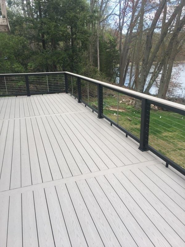 Gray composite deck with black railing and glass panels, overlooking a body of water and trees.